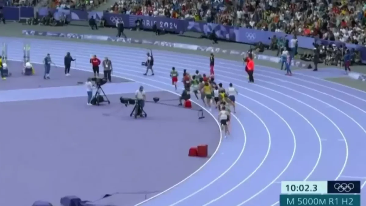 Um operador de câmera passeia casualmente pela pista olímpica enquanto a corrida masculina de 5.000 metros estava acontecendo. (X/@herrerandres4)