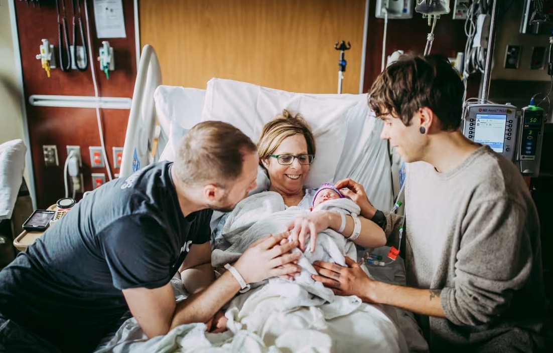 Matthew Eledge, à esquerda, sua mãe, Cecile, e seu marido, Elliot Dougherty, recebem a bebê Uma